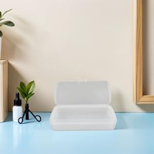 White tissue box dispenser on light blue surface near potted green plant, positioned against neutral wall with framed artwork.