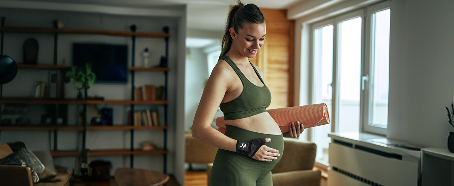 Woman in green activewear holding a yoga mat and water bottle in a home setting with bookshelves and windows visible in the background.