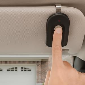 A hand presses the button on the remote, which is conveniently clipped to a car&amp;#39;s sun visor.