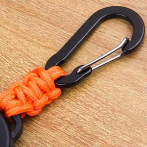 Black carabiner with bright orange paracord attachment shown against a wooden surface.