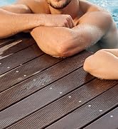 Close-up of wet arms resting on wooden deck boards near water, suggesting a pool or beach setting. Water droplets visible on skin.