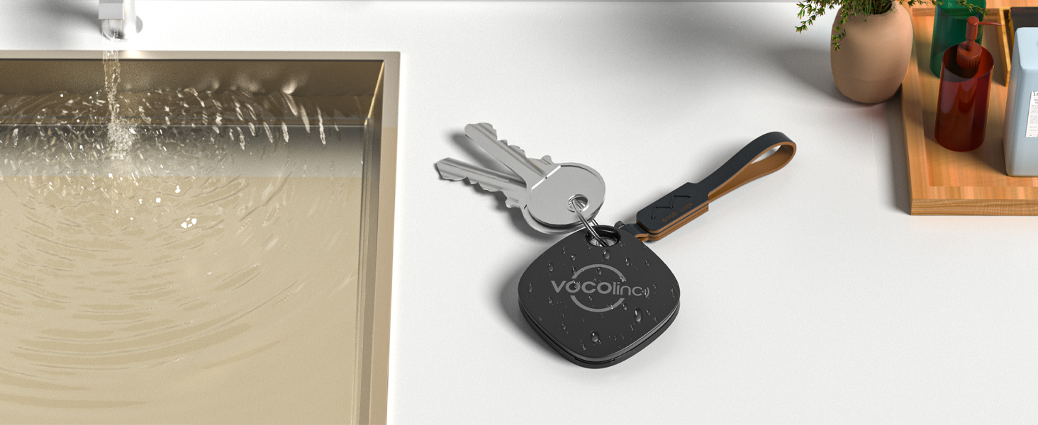 Key finder device attached to keyring with keys. Nearby steamy glass surface and wooden object visible in background.