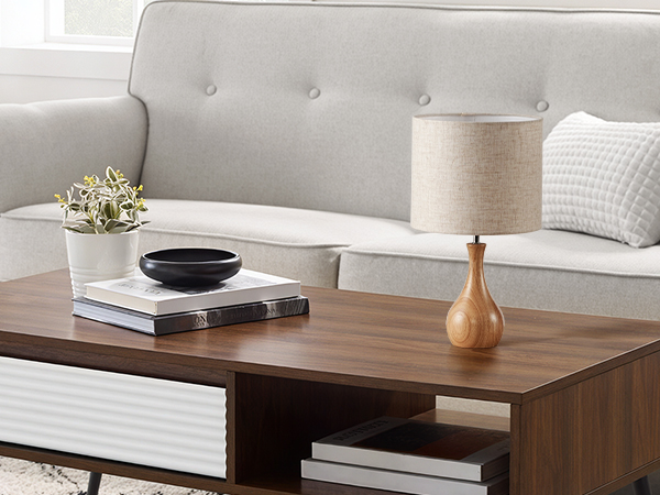 Modern living room setting with light gray tufted sofa, wooden coffee table, table lamp with wooden base, and decorative items including books and small plant.