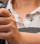 Close-up of a hand holding a metallic smartwatch or fitness tracker. The device's screen is visible on the wearer's wrist.