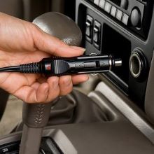 Closeup image of a person's hand plugging a power cord into a vehicle's 12V receptacle
