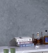 Grey concrete or stone wall background with small green containers and various bottles and books arranged in a vignette style at the bottom edge.