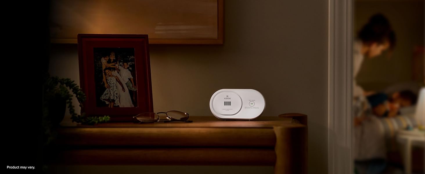 Kidde AA battery carbon monoxide detector sitting on table at nighttime, 10 year expiration, desktop