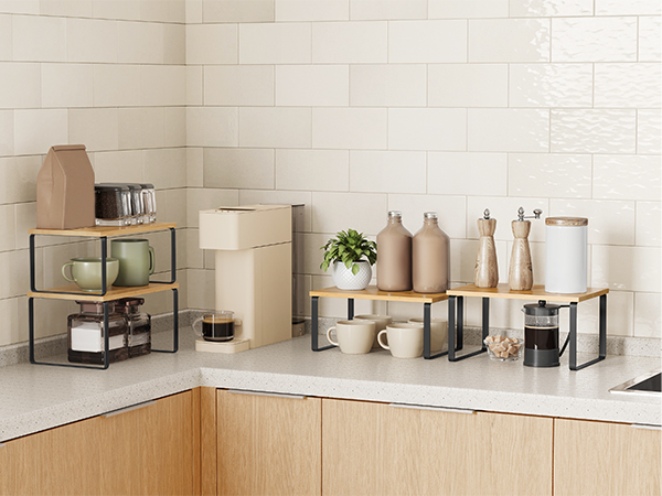 Kitchen counter organization featuring tiered shelves, storage containers, and decorative items. Wooden cabinets below and white tiled wall in background.