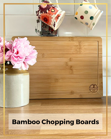 Bamboo chopping board on a kitchen counter with mugs hanging and flowers in a vase