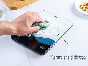 Text reads 'Tempered Glass'. Shows hand cleaning a glass surface with blue tint and measuring scale, next to what appears to be food items.