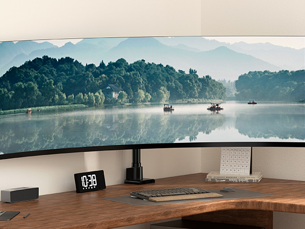 Ultrawide curved monitor setup on wooden desk, displaying serene lake landscape with mountains, accompanied by digital clock and keyboard.