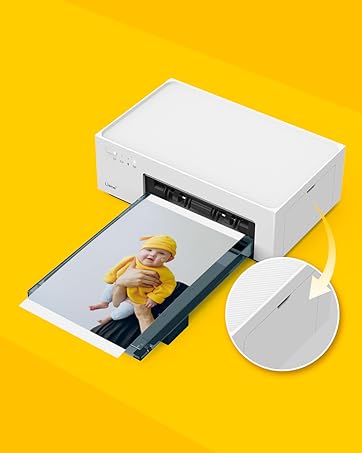 Compact white photo printer on yellow background, printing image of baby. Printer has minimalist design with rounded edges.