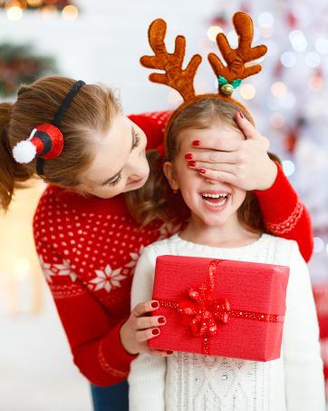 Holiday scene with red wrapped present featuring a bow, and festive reindeer antler decorations visible in a Christmas setting.