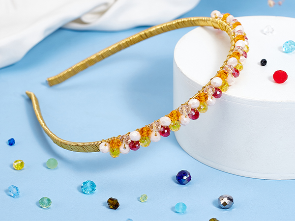 Gold-toned headband adorned with small multicolored beads and crystals, displayed on light blue background with scattered decorative gems.