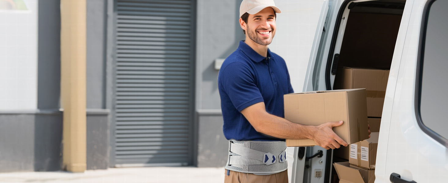 Delivery person in blue polo shirt and cap carrying cardboard box from white van. Industrial loading area visible in background.