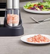Electric salt grinder with pink Himalayan salt inside clear chamber, shown with salad and plate of ground salt on gray surface