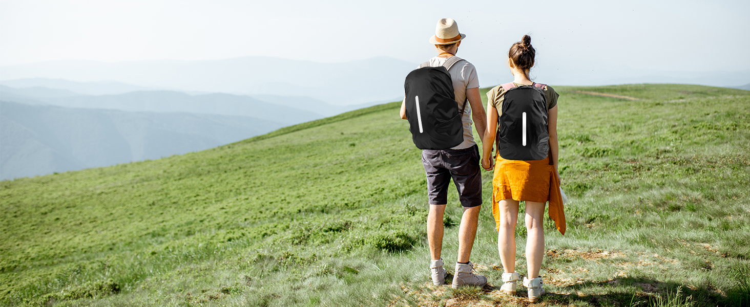 Two people standing on grassy hilltop overlooking water. Wearing casual clothing and facing away from camera towards scenic view.