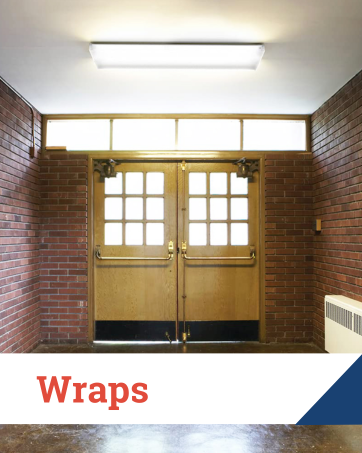 Ceiling wrap light fixture above double wooden doors in a brick school or public building hallway.