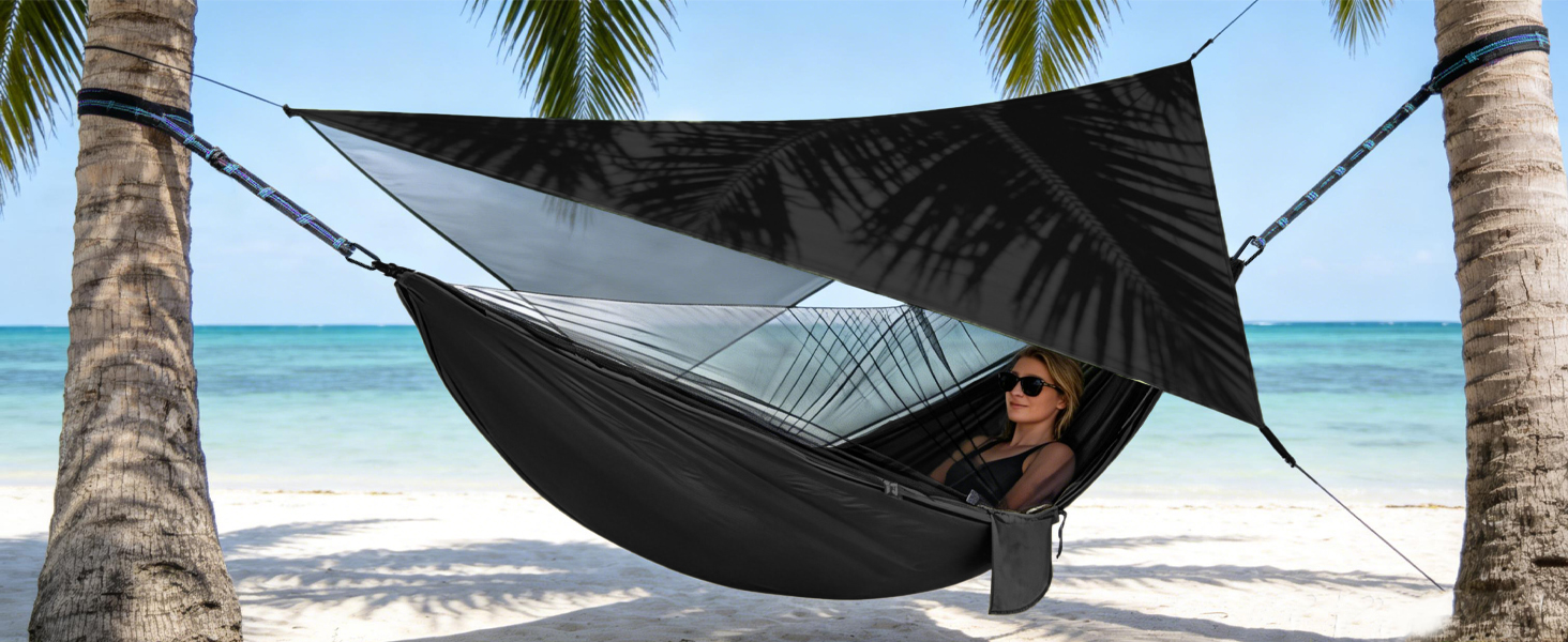 Black hammock suspended between palm trees on tropical beach with ocean view.