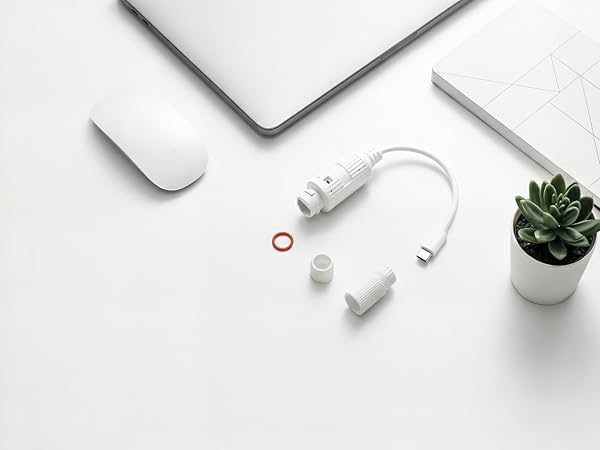 Flat lay composition showing white computer accessories: mouse, keyboard, charging cable with USB connector, earbuds, and small potted succulent plant on white surface.
