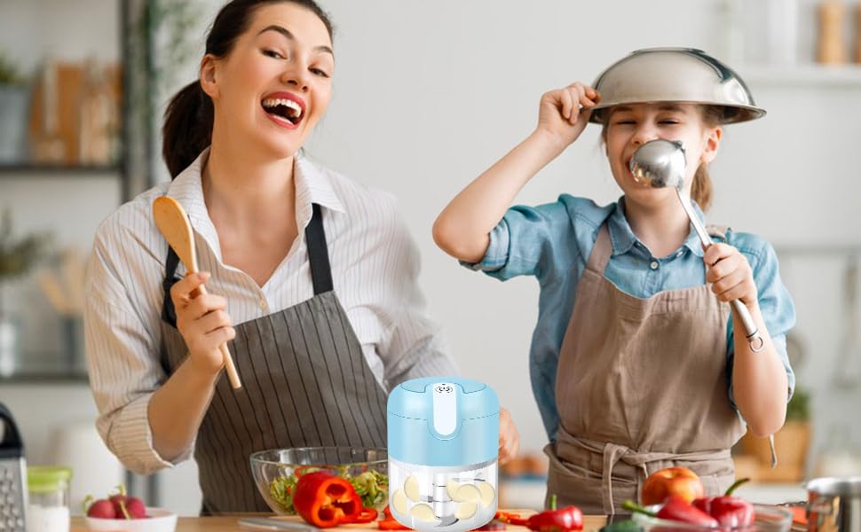 Two people in kitchen aprons preparing food at a counter with fresh vegetables and a jar visible. Both are in playful cooking poses.