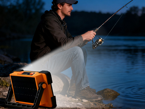 Angler fishing at river at night with portable LED work light illuminating the bank