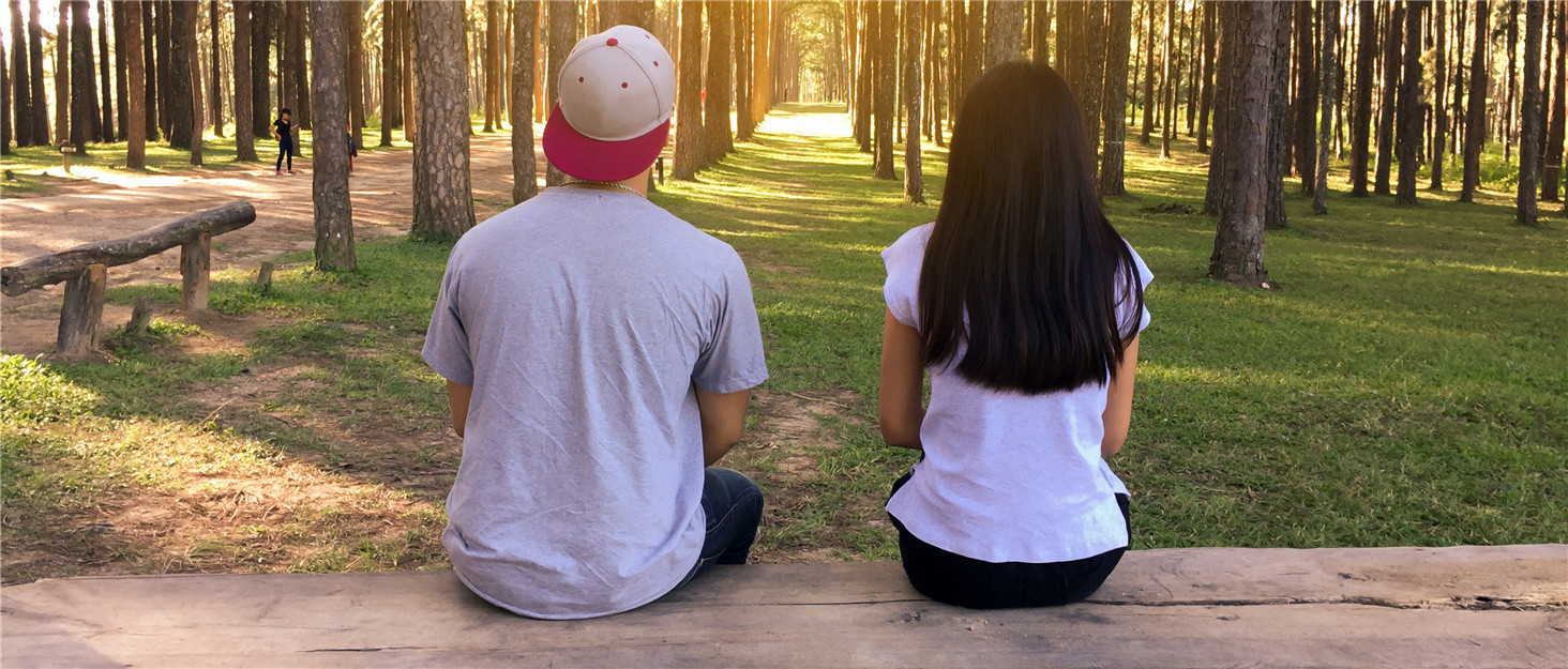 a man and a woman sitting on a bench in a forest.