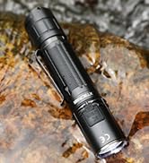 Tactical flashlight with black metal construction photographed on rocky terrain, featuring visible grip texture and compact design.