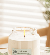 White scented candle in clear glass container with soft, warm lighting.