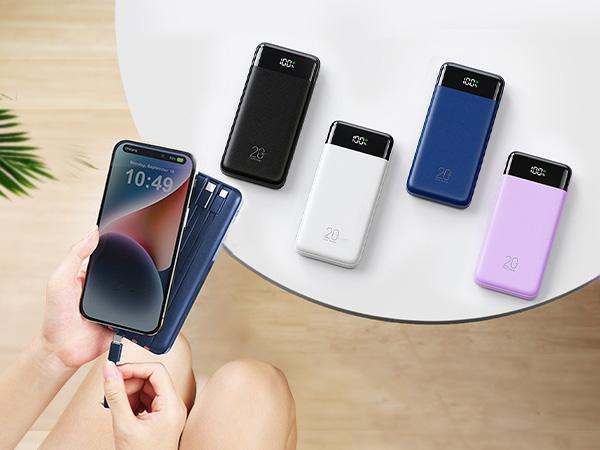 Hand holding smartphone displaying time 10:47 surrounded by five portable power banks in black, white, and pink colors arranged on white curved surface with plant leaf visible.