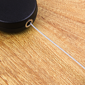 Black retractable cord or measuring tape device on a wooden floor surface.