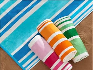beach towels with an alternate stripe design, rolled up on top of sand