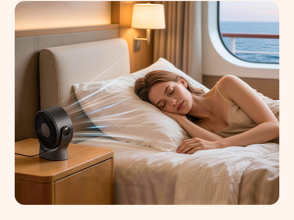 Small portable fan placed on wooden nightstand next to bed in what appears to be a train or ship cabin with window visible.