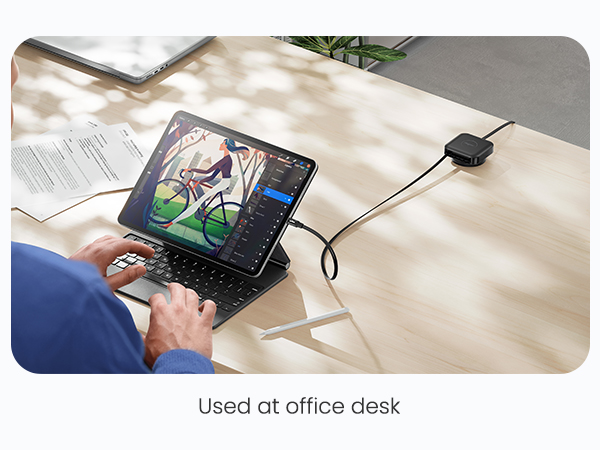 Tablet with detachable keyboard on office desk, displaying colorful digital artwork. Connected to small black device. Stylus visible nearby.