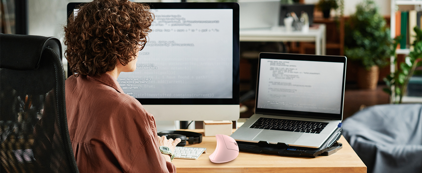 a woman sitting at a desk with a laptop and a monitor.