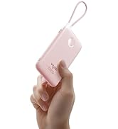 Hand holding a small, rectangular pink device with a wrist strap. Device has a smooth surface with a circular cutout and visible text, suggesting a portable electronic product.