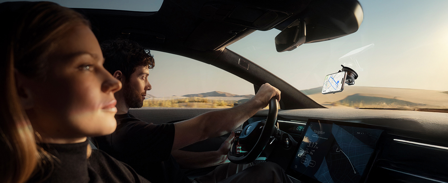 Interior view of a car dashboard and windshield, showing a digital display and steering wheel. Desert landscape visible through the windshield.