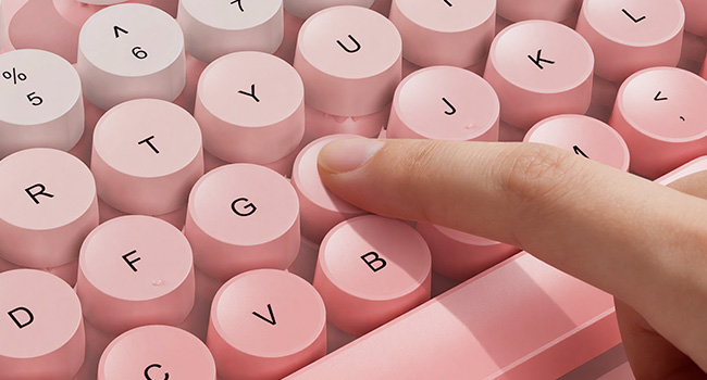 Finger pressing pink round keycaps on wireless keyboard for smooth responsive typing feel