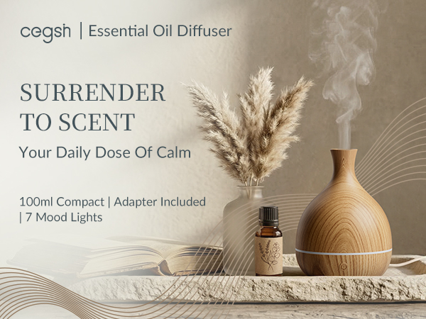 Wood grain vase essential oil diffuser on stone tray with art books and amber glass oil bottle.