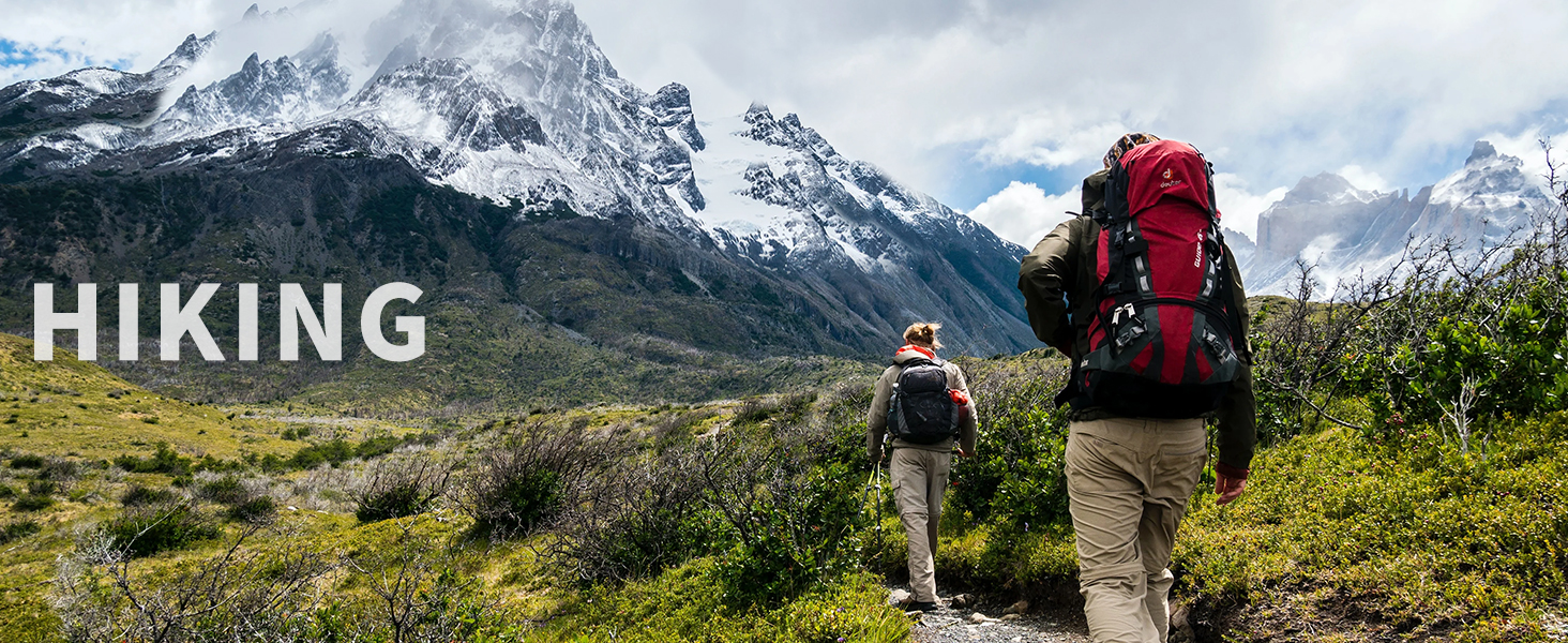 Two hikers with backpacks walking through a grassy field towards snow-capped mountains. Text overlay reads 'HIKING'.