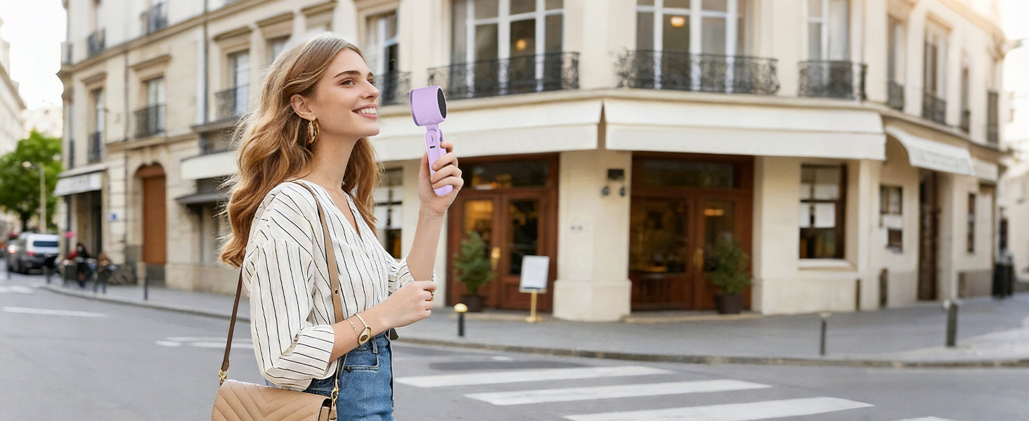 Woman walking in city holding purple handheld fan stylish mini fan for holiday travel cooling