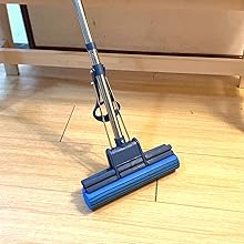 Blue and gray sponge mop with metal handle on wooden floor, positioned next to light-colored wooden furniture.