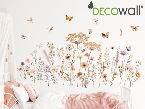 Text reads 'DECOwall'. Decorative wall decal featuring delicate wildflowers, butterflies, and botanical elements in soft peach and pink tones against white background with pink cushions visible.