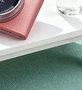 Close-up product photo showing corner of pink leather item against white surface and green textured background with glass container visible.