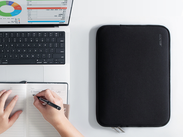 a person writing on a notepad next to a laptop.