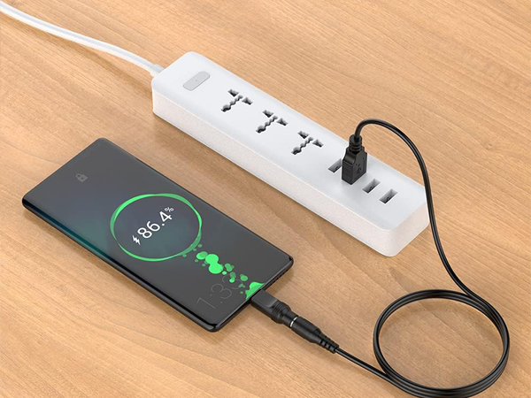 White power strip with multiple outlets and USB ports on wooden surface. Smartphone connected, displaying green circular charging indicator at 86.4%.