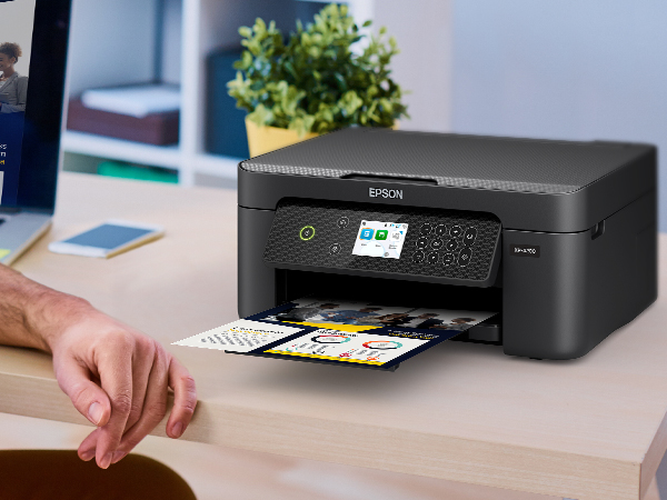 Black Expression Home XP-4200 printer sitting on desk with colorful business flyer in output tray.