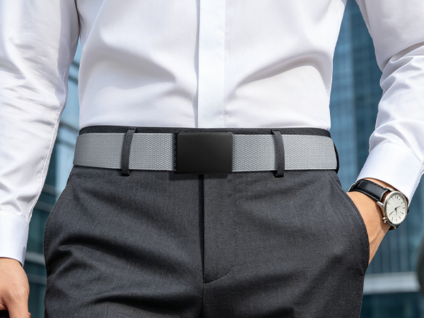 Person wearing light blue shirt holding dark gray flat-front trousers at waist, demonstrating fit and style of men's dress pants.