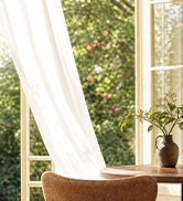White modern lounge chair positioned near sunlit window with green foliage visible outside.