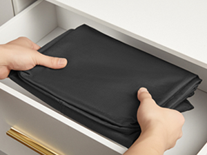 Hands placing or removing a black rectangular device into what appears to be a storage drawer or compartment.